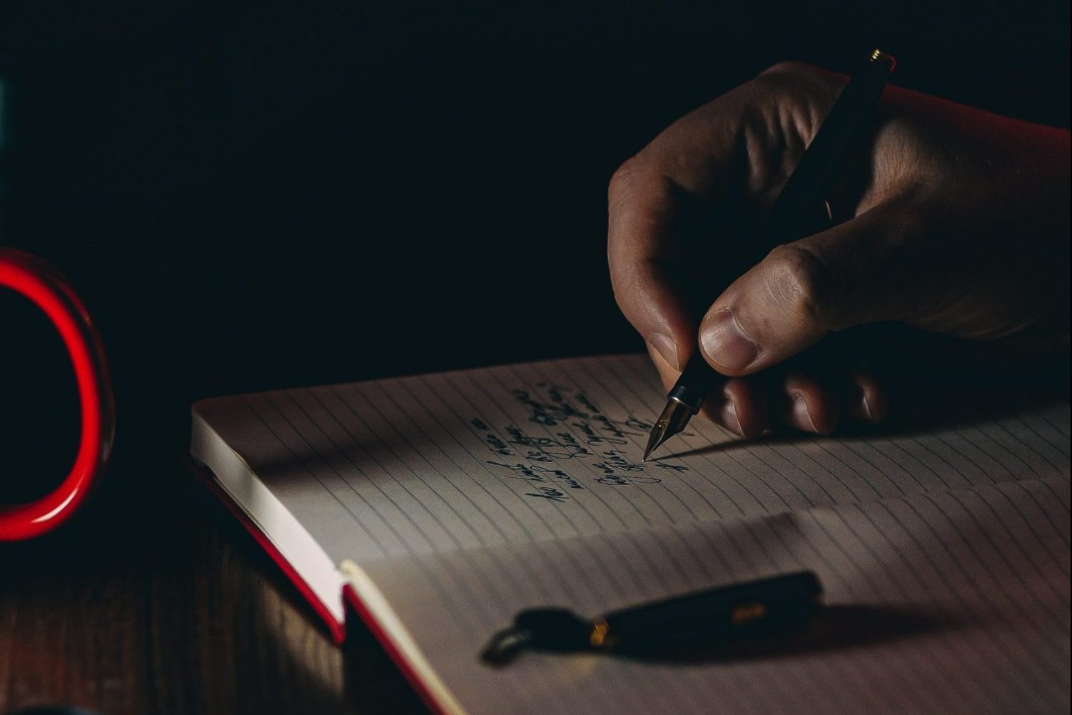 in article about college writing workshop, a hand writing into a notebook